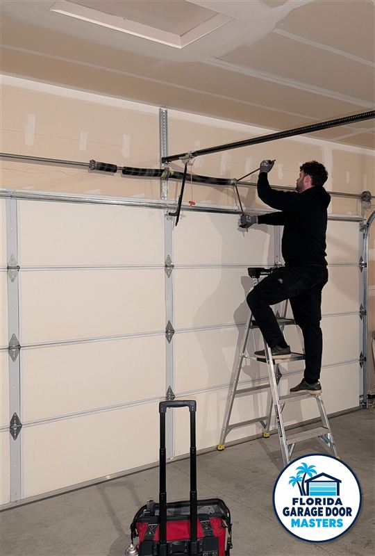 Technician on a ladder repairing garage door cable drum and bracket
